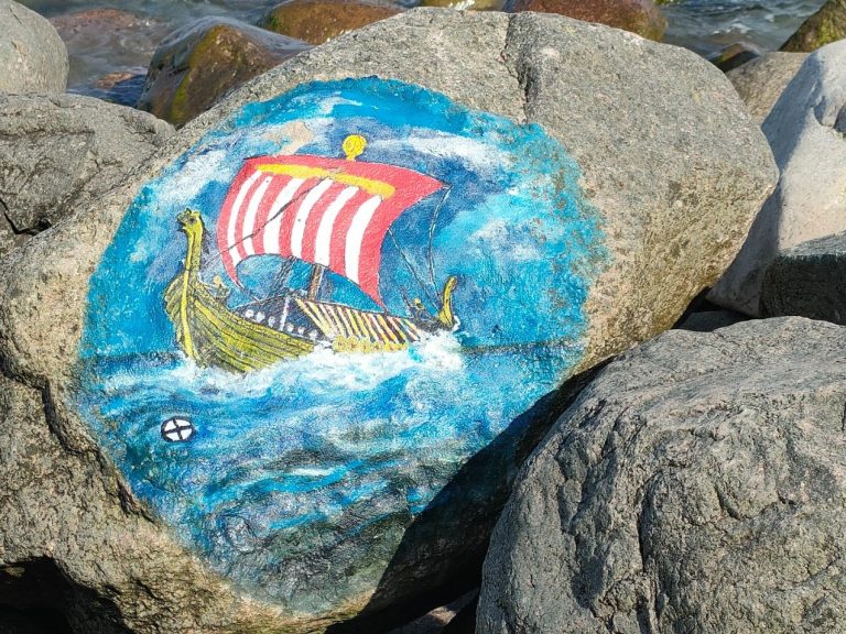 Bunt bemalter Stein mit einem Wikingerschiff, das durch blaue Wellen segelt.