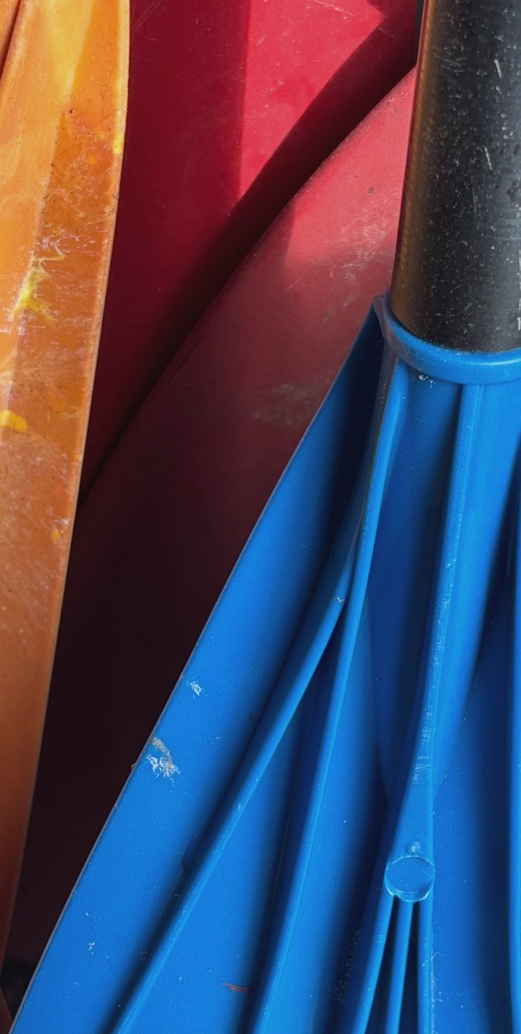 Bunte Paddel in Orange, Rot und Blau, eng nebeneinander angeordnet.